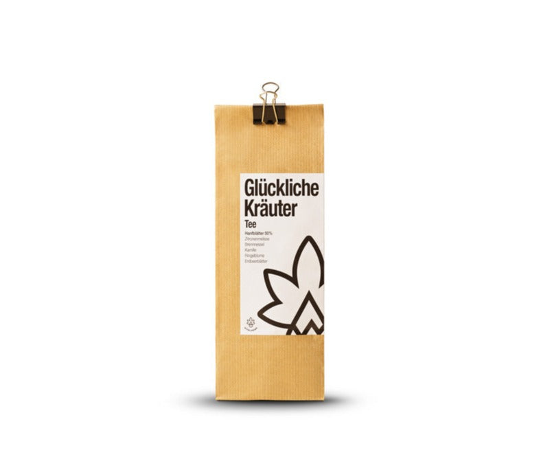 Bio-Hanftee mit Kräutern: Kraftpapier-Packung ‚Glückliche Kräuter Tee‘ mit Klammer vor weißem Hintergrund
