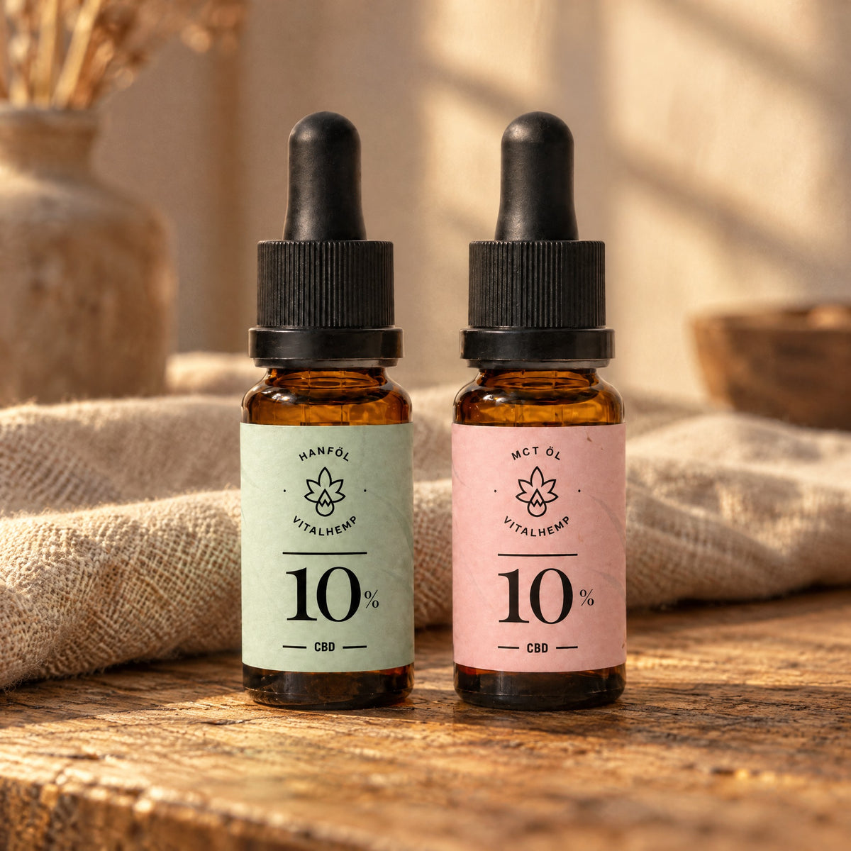 Trägeröl-Probe: CBD-Öl 10 % mit mintgrünem Etikett (Bio-Hanföl) und mit roséfarbenem Etikett (Bio-MCT-Öl) auf Eichenholz und Leinen