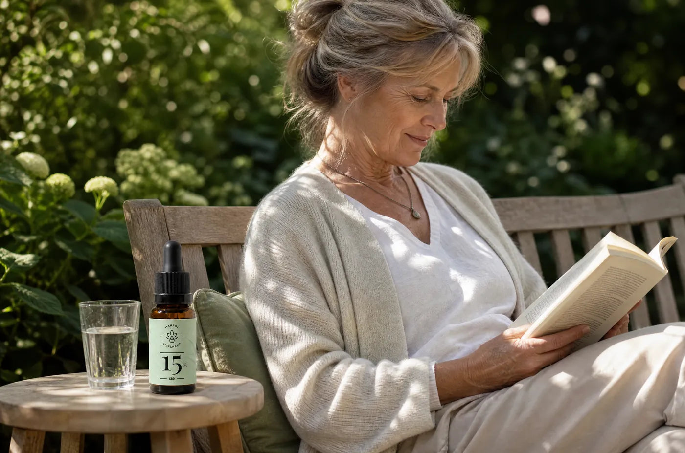 Frau auf einer Gartenbank mit einem Buch und einer VITALHemp CBD-Öl-Flasche 15 Prozent