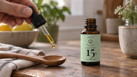 Flasche VITALHemp Pure 15 % CBD-Öl, die Pipette hält einen einzelnen Tropfen über einem Holzlöffel, Symbolbild für Bioverfügbarkeit.