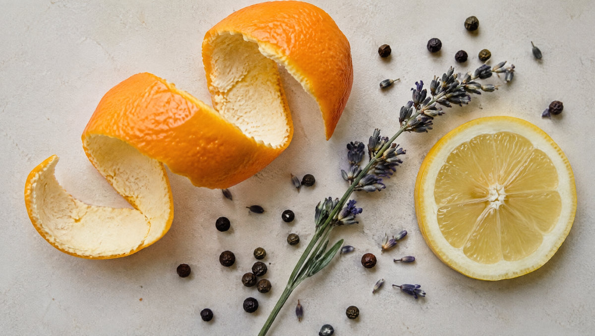Draufsicht auf Orangenschale, Lavendel, Pfefferkörner und eine Zitronenscheibe als Stillleben.