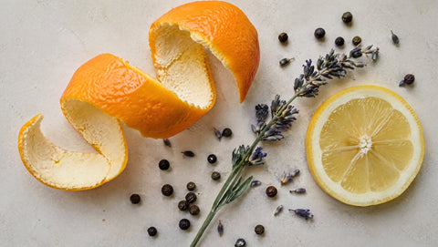 Draufsicht auf Orangenschale, Lavendel, Pfefferkörner und eine Zitronenscheibe als Stillleben.