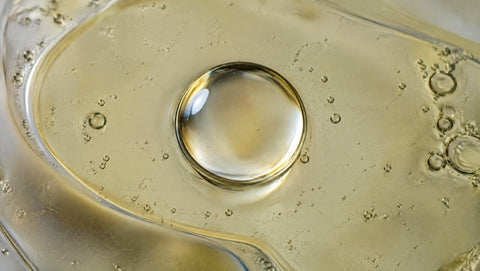 Makroaufnahme eines Wassertropfens auf einer Ölfläche von oben.