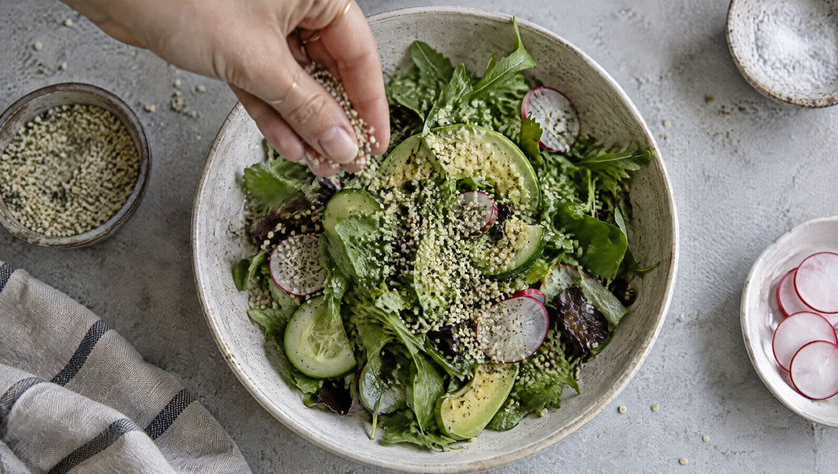 Hand streut geschälte Hanfsamen über einen grünen Salat