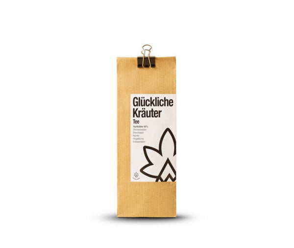 Bio-Hanftee mit Kräutern: Kraftpapier-Packung ‚Glückliche Kräuter Tee‘ mit Klammer vor weißem Hintergrund