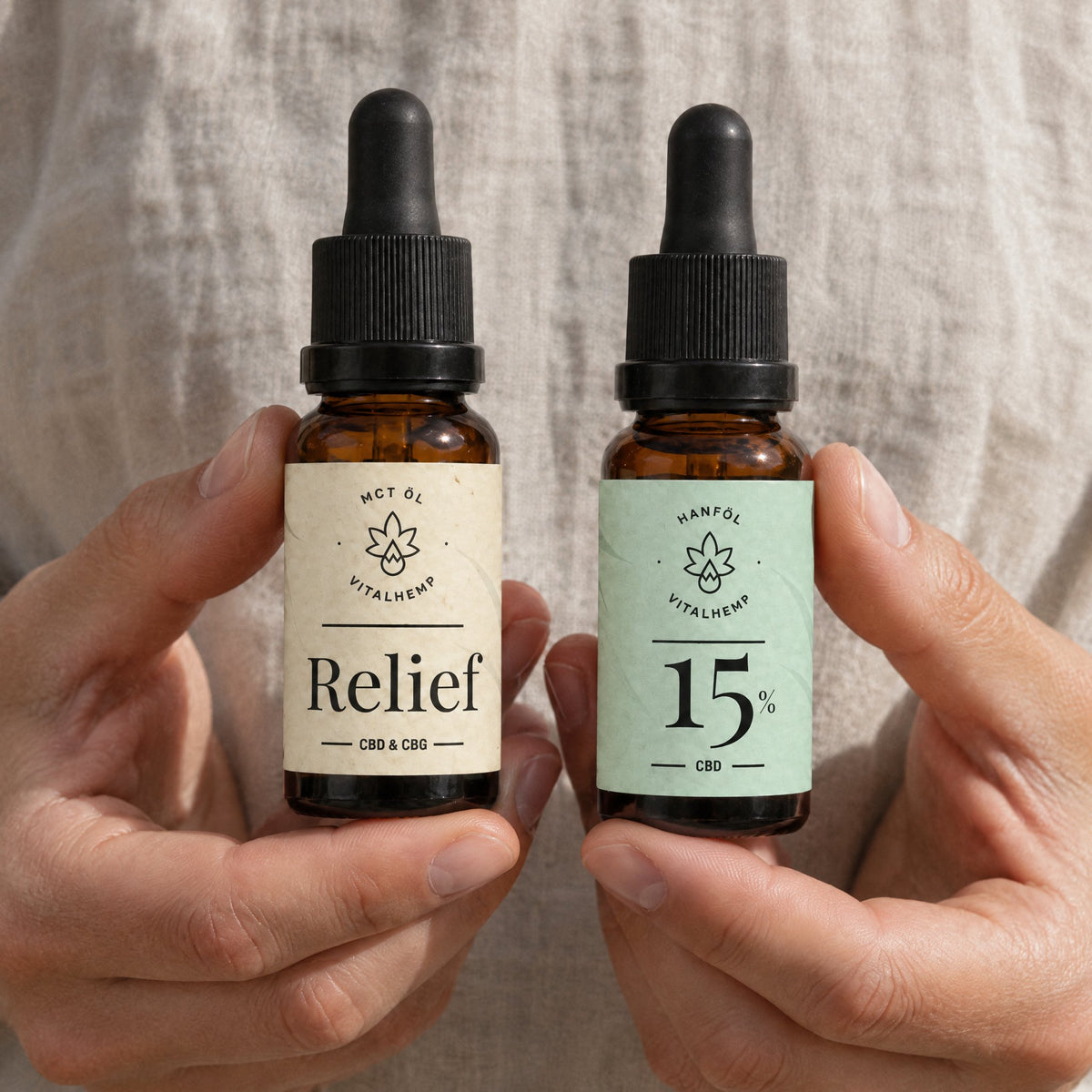 Zwei Haende halten je eine Flasche, VITALHemp Relief und CBD-Oel 15 Prozent, vor Leinenstoff