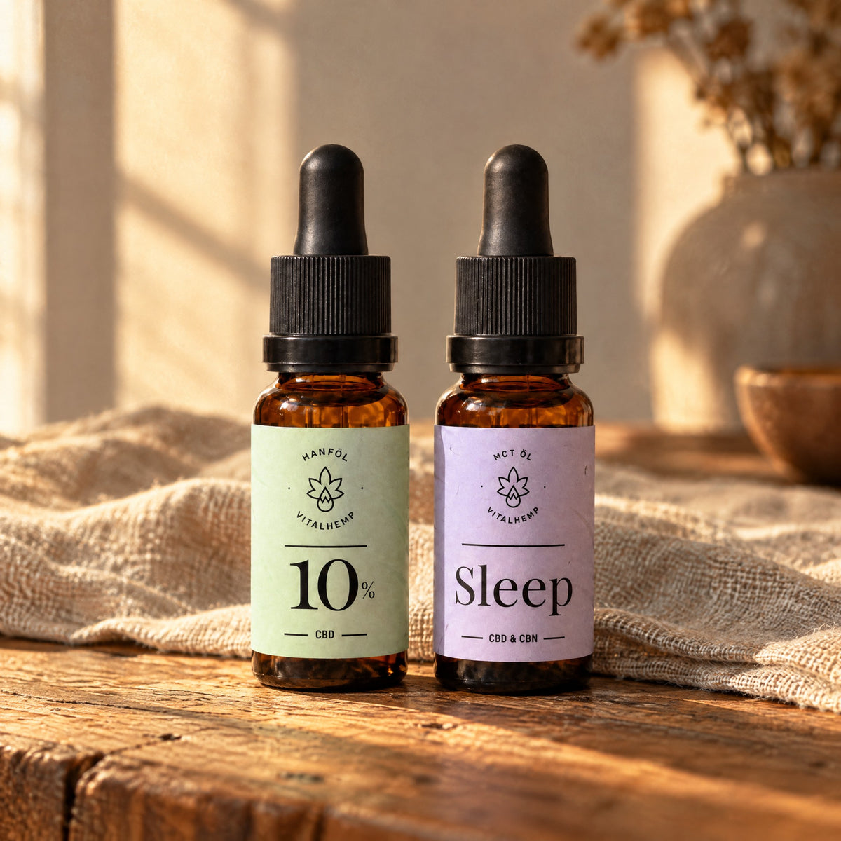 Tag-&-Abend-Set: Flasche CBD-Öl 10 % mit mintgrünem und Flasche Sleep-Öl mit lilafarbenem Etikett auf Eichenholz und Leinen