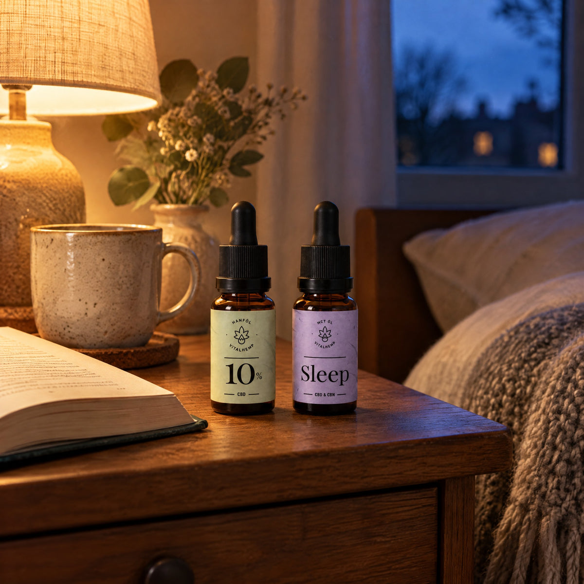 CBD-Öl 10 % und Sleep-Öl auf einem Nachttisch neben Lampe, Tasse und Buch am Abend